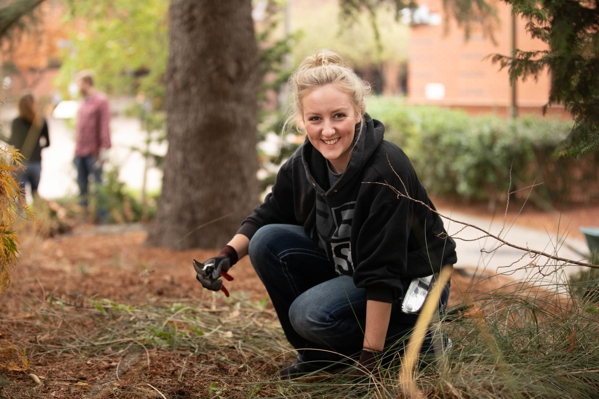 A student with clippers picking up branches on the ground